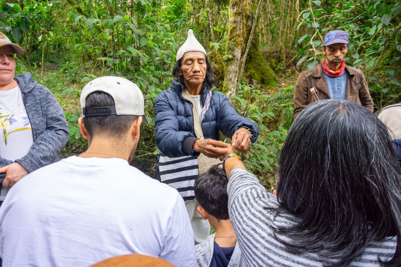 Un mayor indígena entrega una pulsera de hilo a los visitantes durante una ceremonia en el bosque